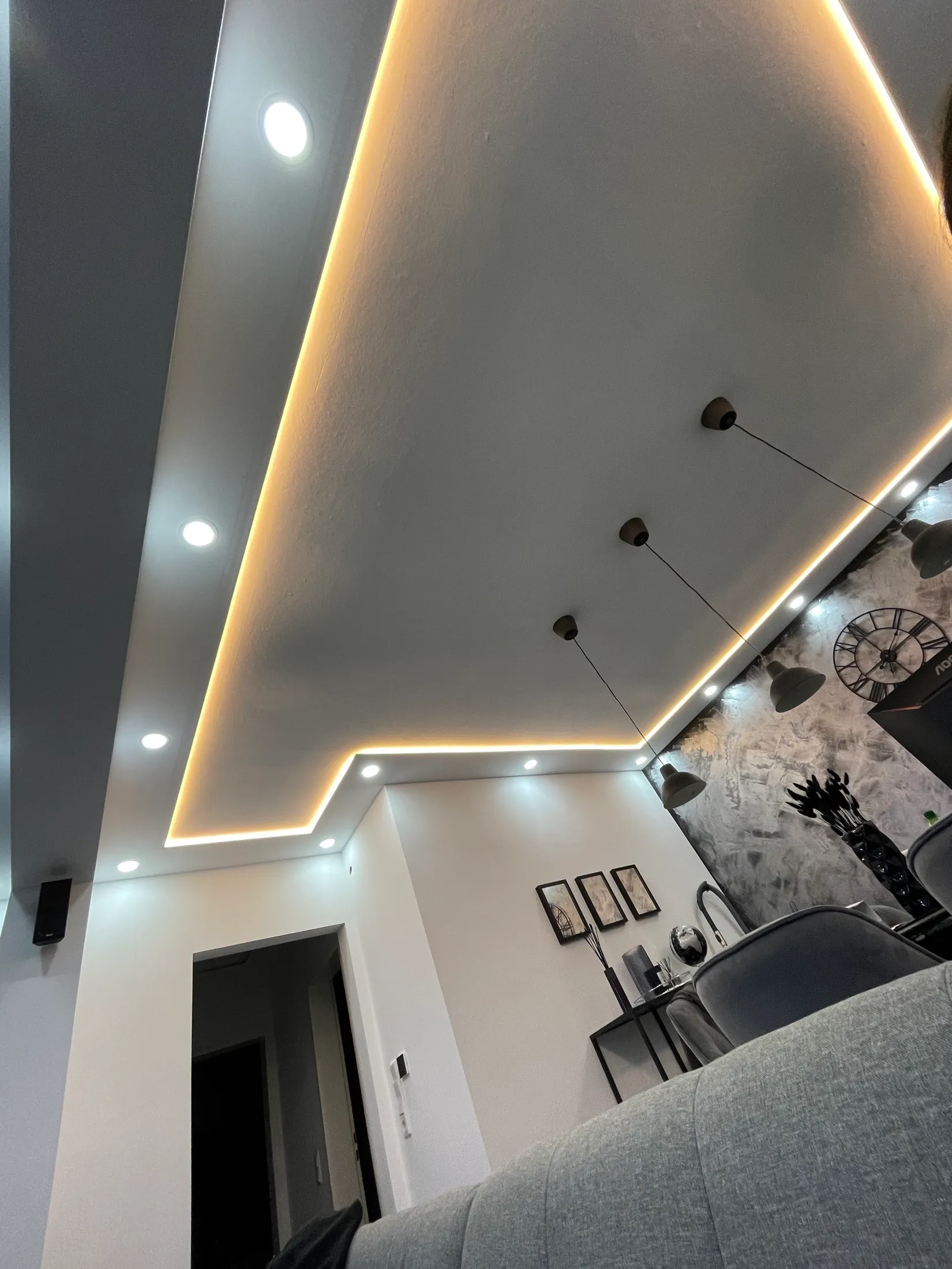 Wohnzimmer mit abgehängter Decke, indirekter Beleuchtung und grauer Dekorwand