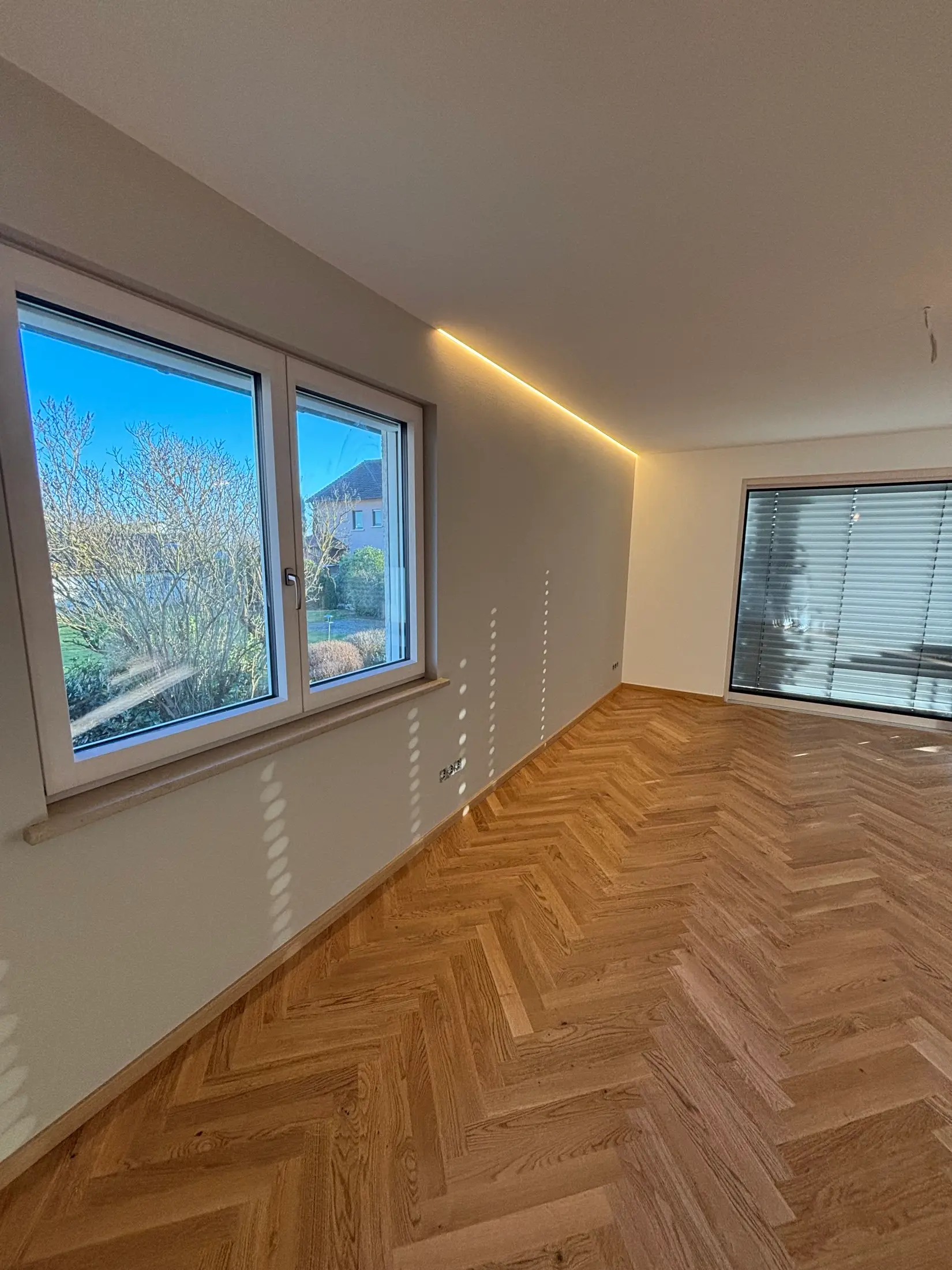 Fertig renoviertes Zimmer mit weißen Wänden, indirekter LED-Deckenbeleuchtung und Eichenparkett