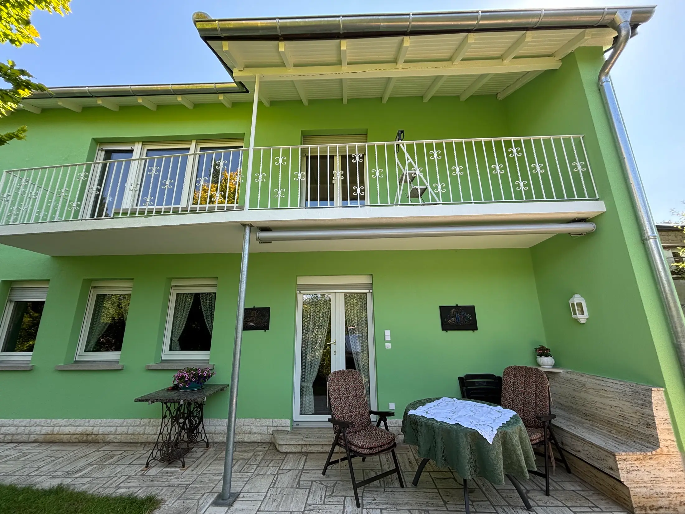 Fertig grün gestrichene Gartenfassade mit weißem Balkongeländer und Terrasse