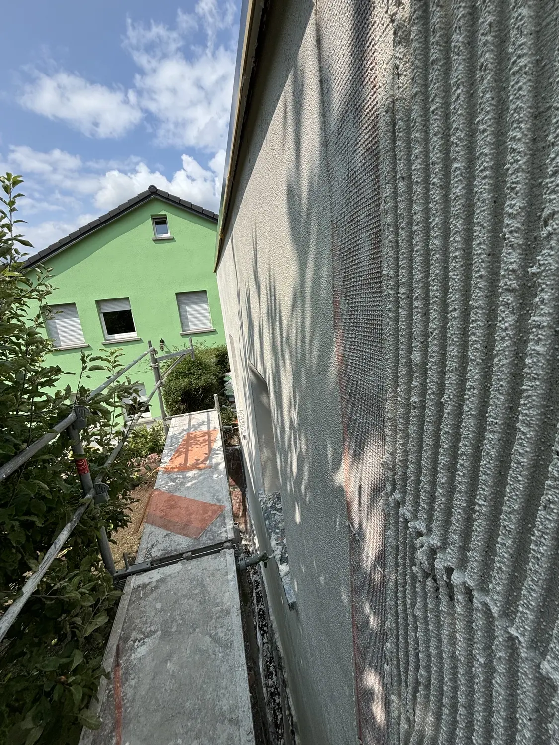 Frischer Armierungsputz mit Gewebeeinlage an einer Außenwand neben dem Gerüst